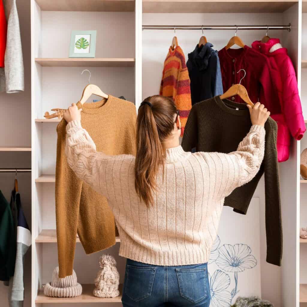 Holding up sweaters in front of a closet