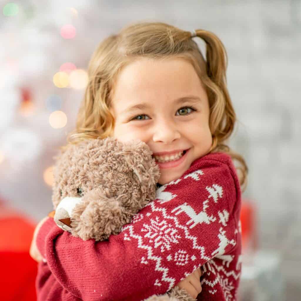 Young girl in a holiday sweater hugging a bear